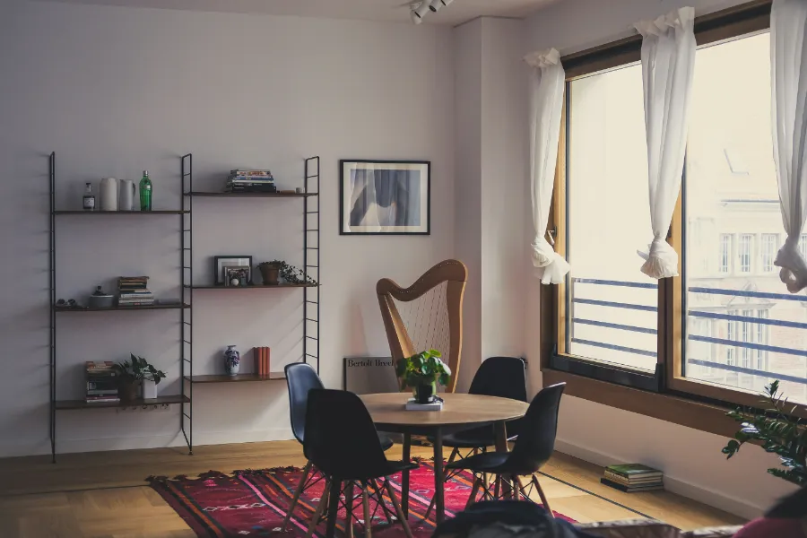Jasne wnętrze mieszkania z drewnianym stołem, krzesłami, półkami na książki i roślinami